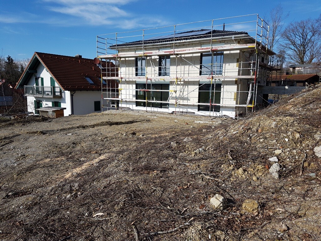 Modernes Haus im Bau mit Gerüst, unbefestigtem Hof und angrenzenden Gebäuden im Hintergrund