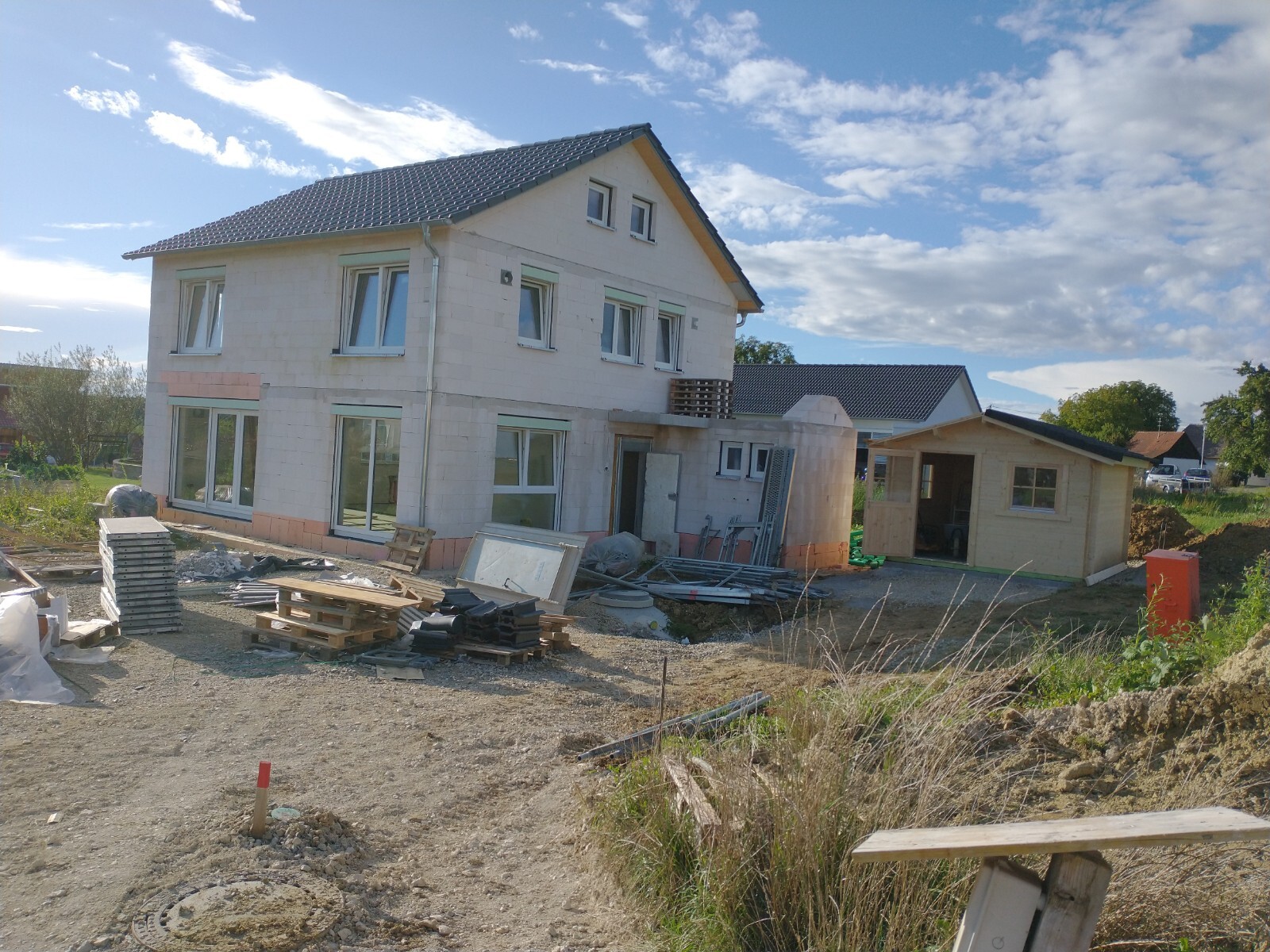 Im Bau befindliches zweistöckiges Haus mit Baustellenmaterialien, Paletten und Bauholz.