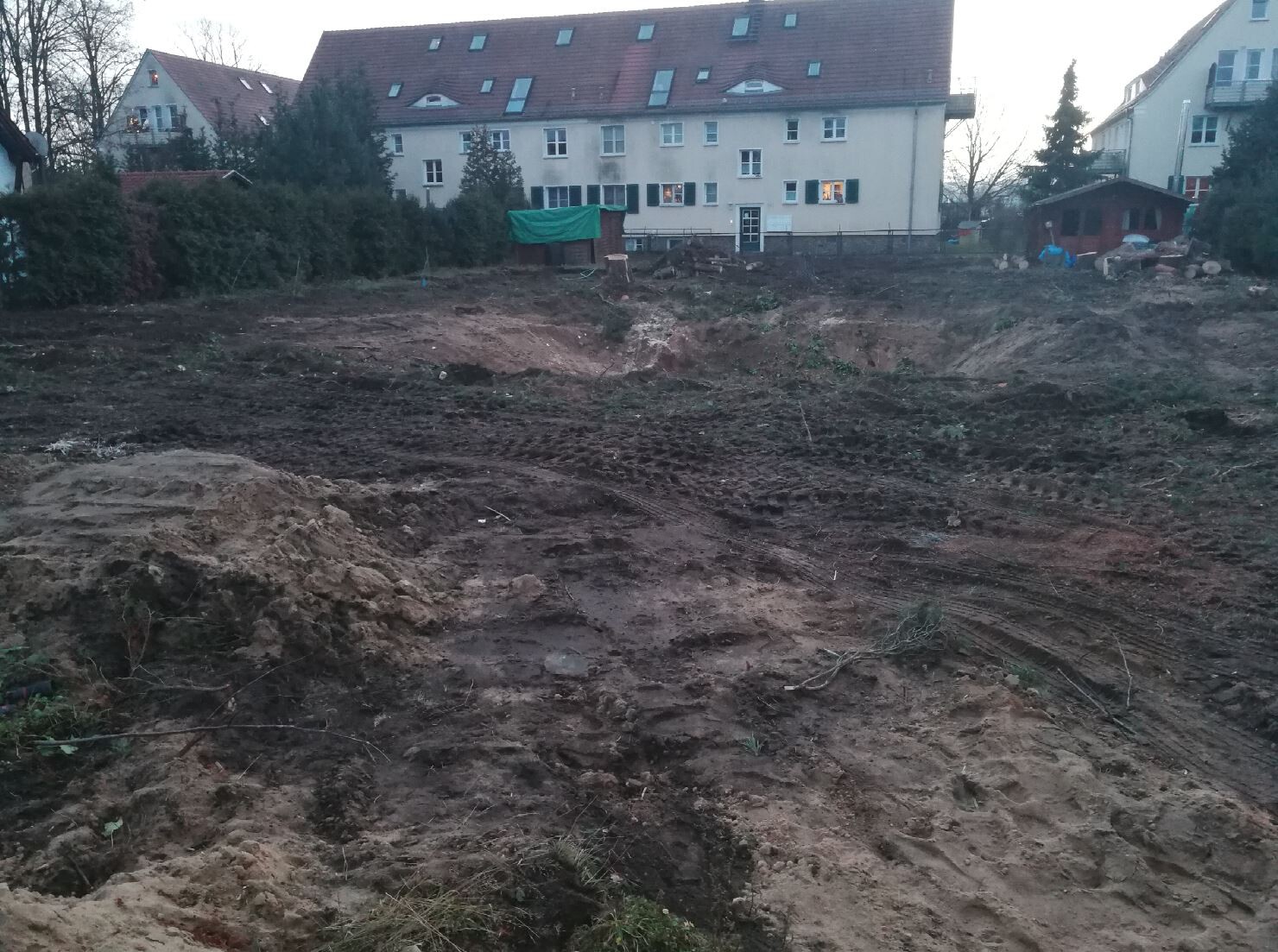 Baugrundstück mit Erdehaufen und Spuren von Baumaschinen vor Wohngebäuden.