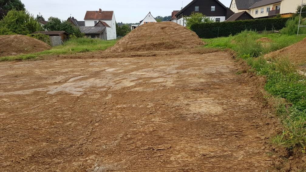 Leeres Baugrundstueck mit Erdmassen und Hausern im Hintergrund, Erdarbeiten sichtbar