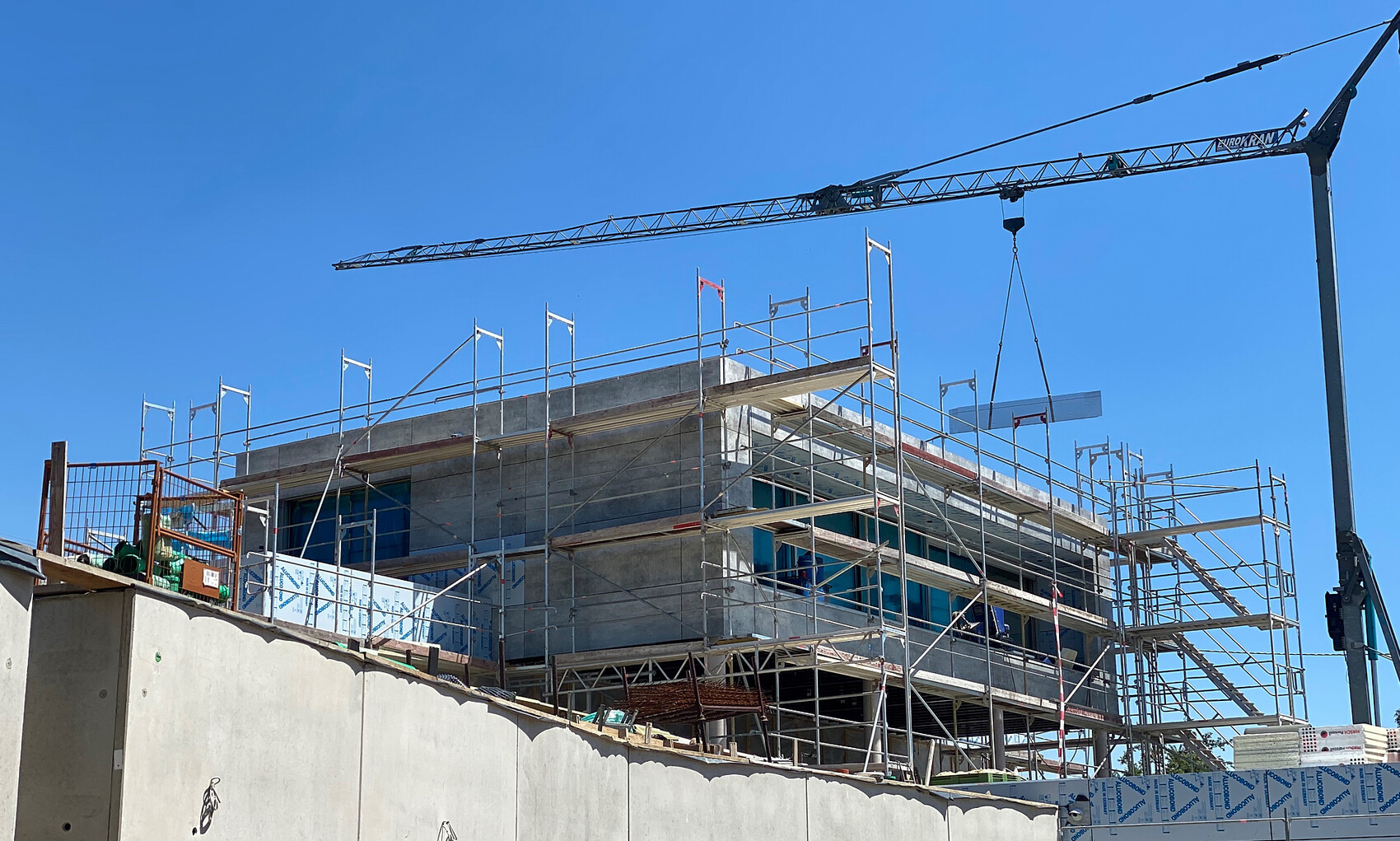 Baustelle mit Gerüst um ein mehrstöckiges Betongebäude; Kran über dem Bauwerk.