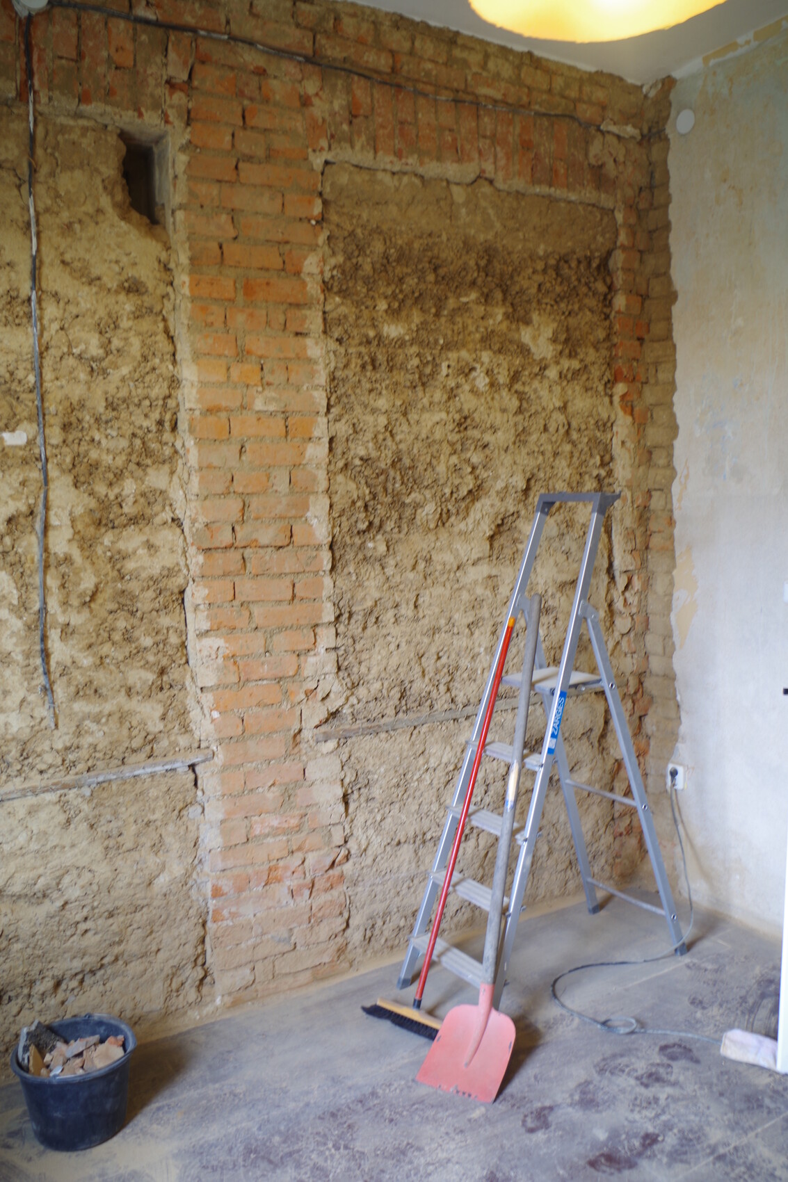 Renovierungsraum mit freigelegter Backsteinwand, Leiter, Besen und Schaufel.