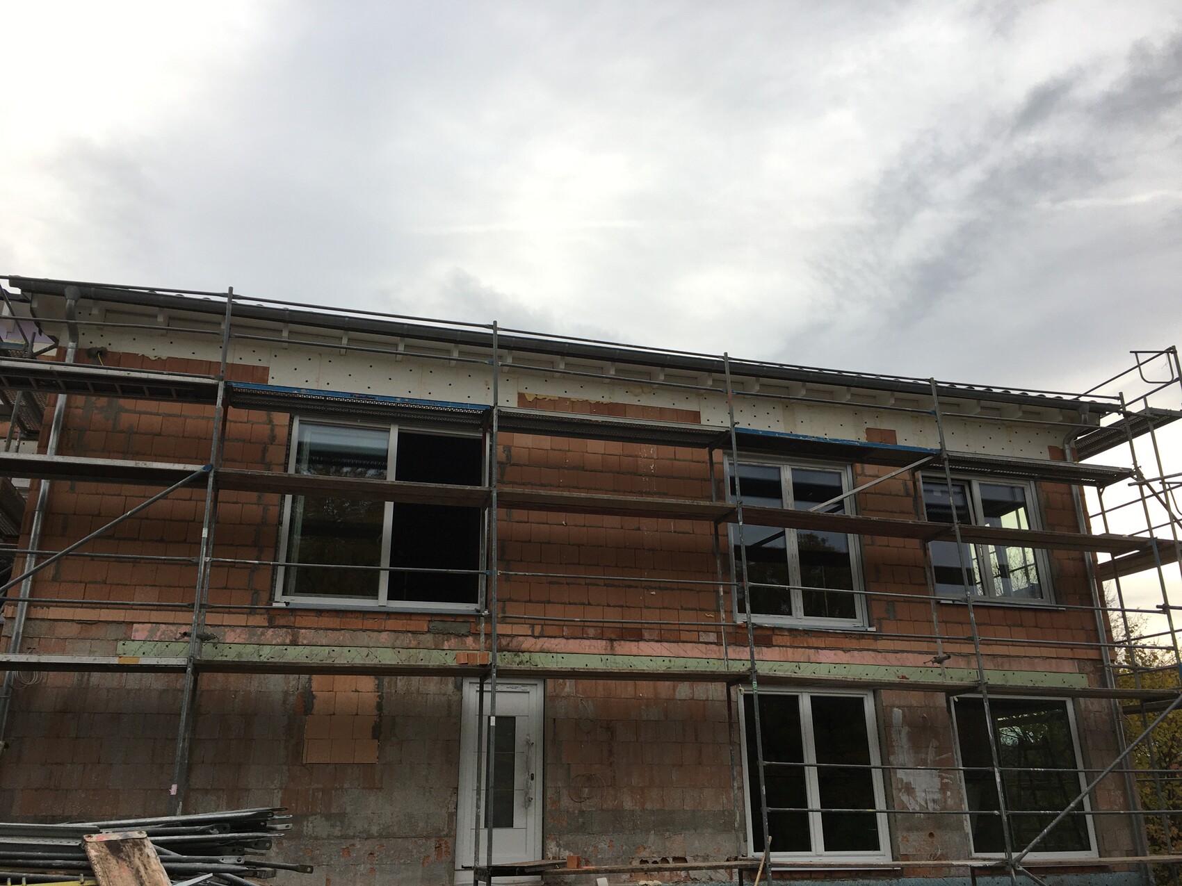 Im Bau befindliches Mehrfamilienhaus mit Gerüst vor roter Ziegelwand und großen Fenstern.
