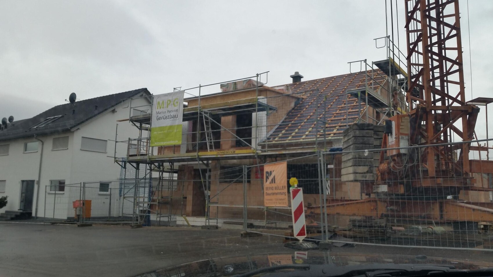 Baustelle mit Gerüst, Kran und Dacharbeiten an einem Haus