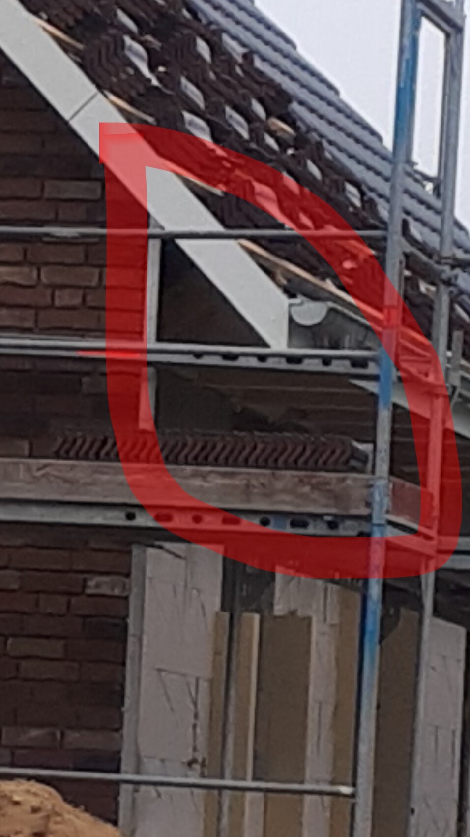 Baustelle an einem Haus: Gerüst, Dachziegel, Backsteinwand und Baumaterialien sichtbar.