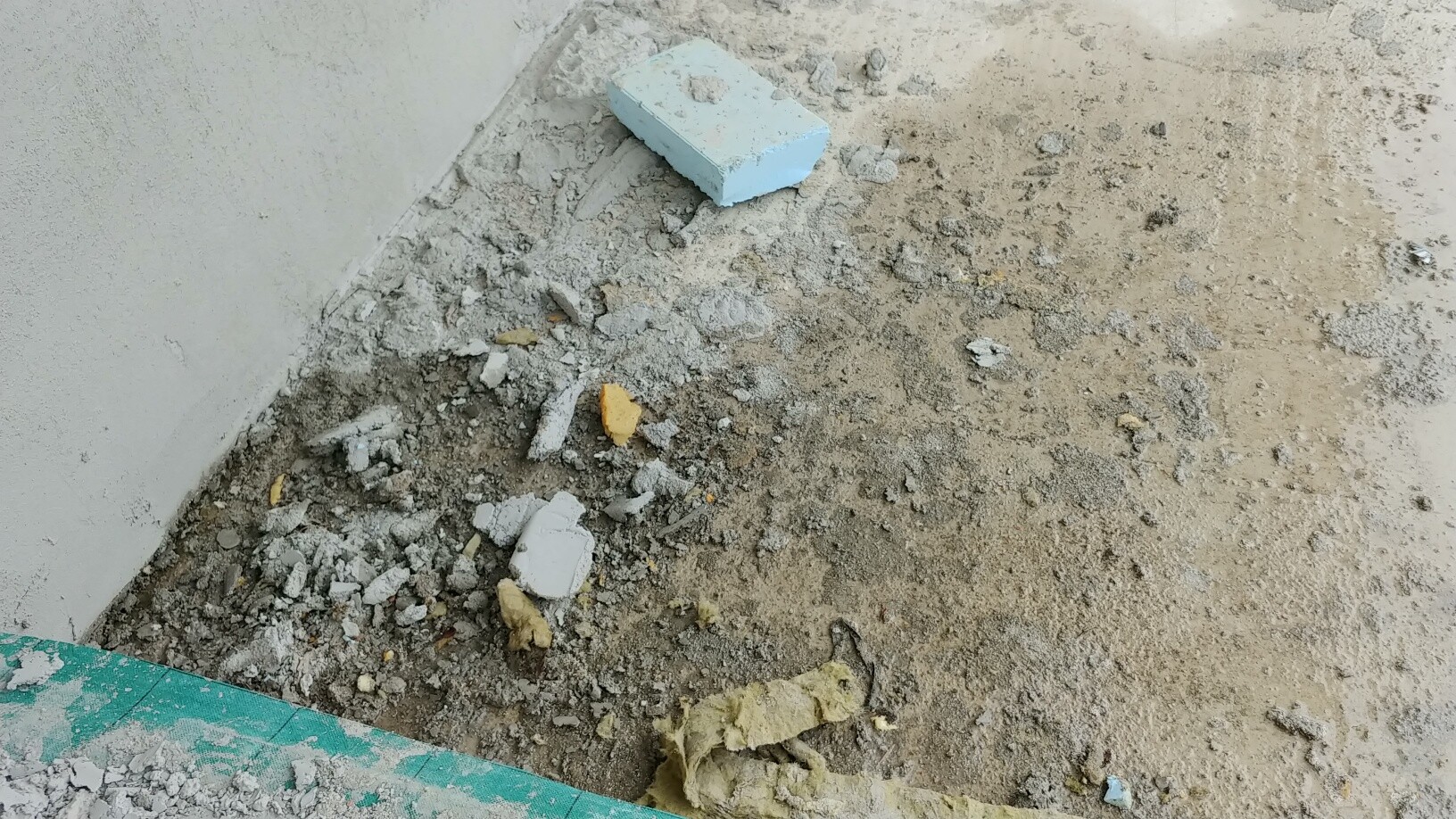 Baustelle mit Betonresten, Schutt und Zementblock neben Rohbauwand