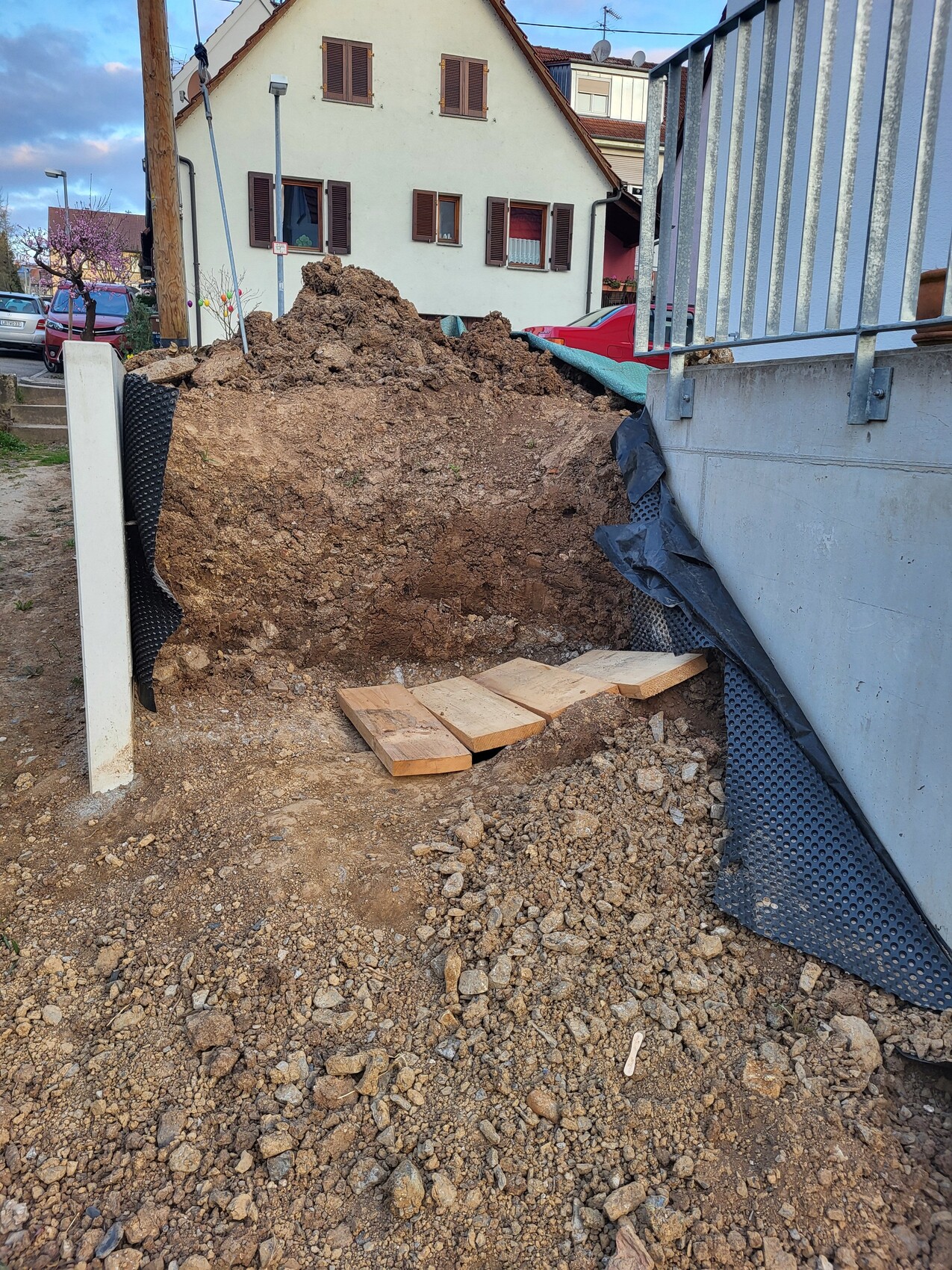 Großer Erdhügel vor Wohnhaus; Bauarbeiten mit Holzbohlen, schwarzer Folie und Kies.
