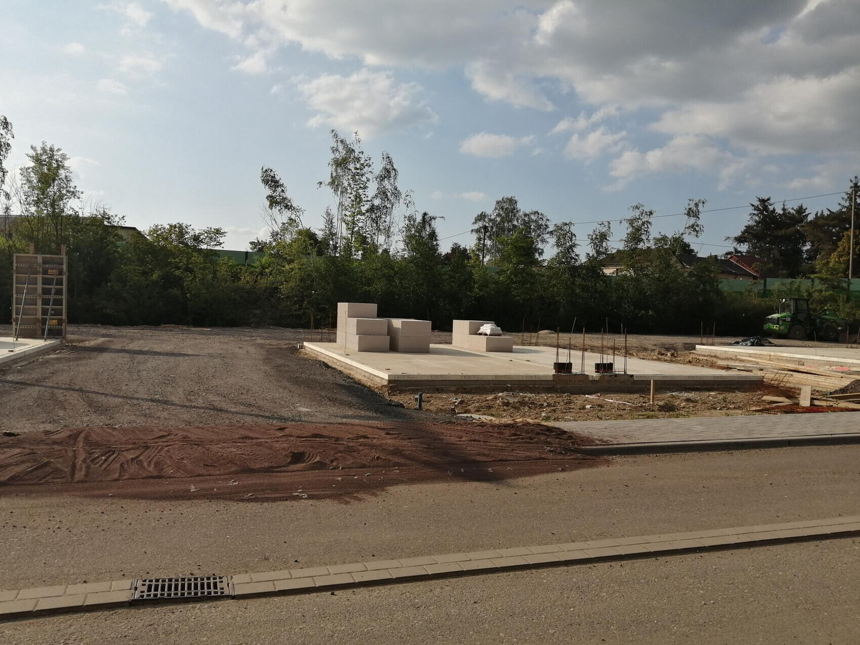 Baustelle mit Betonfundamentplatten, gestapelten Betonblöcken und Baugerät rechts.