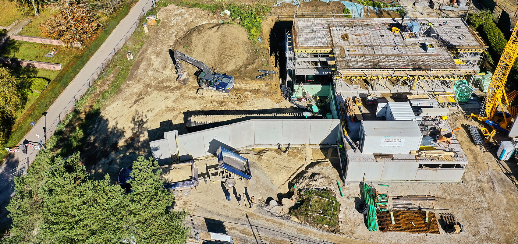 Luftbild einer Baustelle: Bagger, Sandhügel, mehrstöckiges Gerüstbauwerk, Kräne und Materialien
