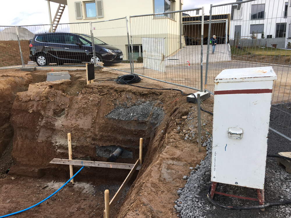 Offene Baugrube mit Fundamentarbeiten, Bauzaun und Kabel auf Baustelle