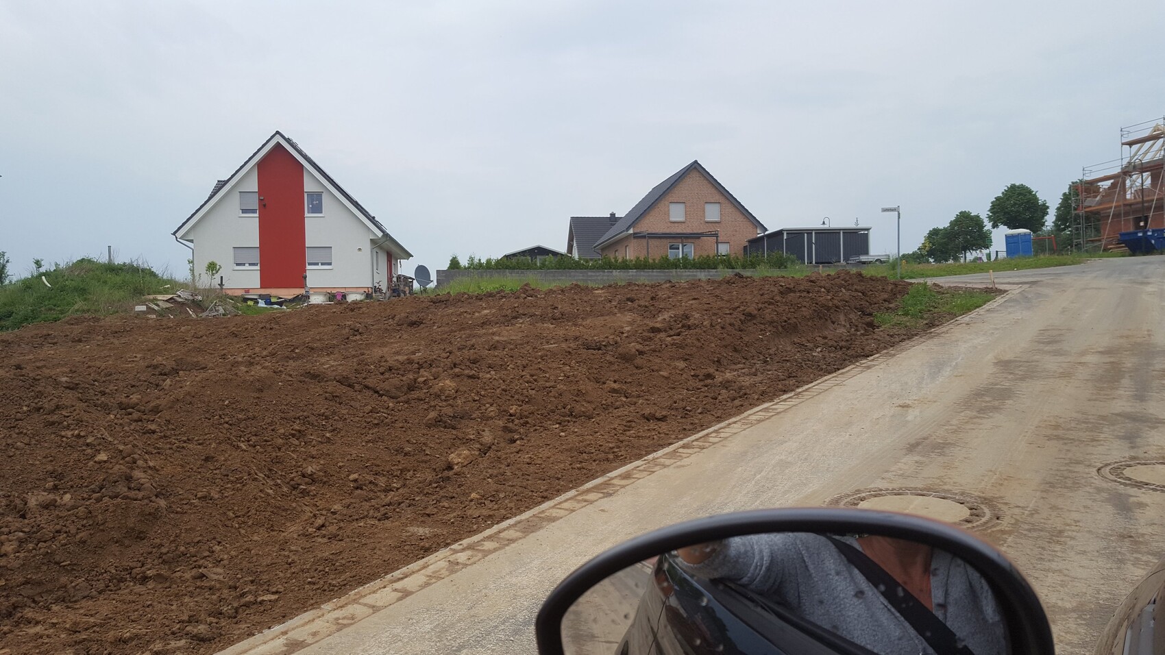 Großer Erdhügel auf einer Baufläche, Häuser im Hintergrund und Straßenzugang rechts