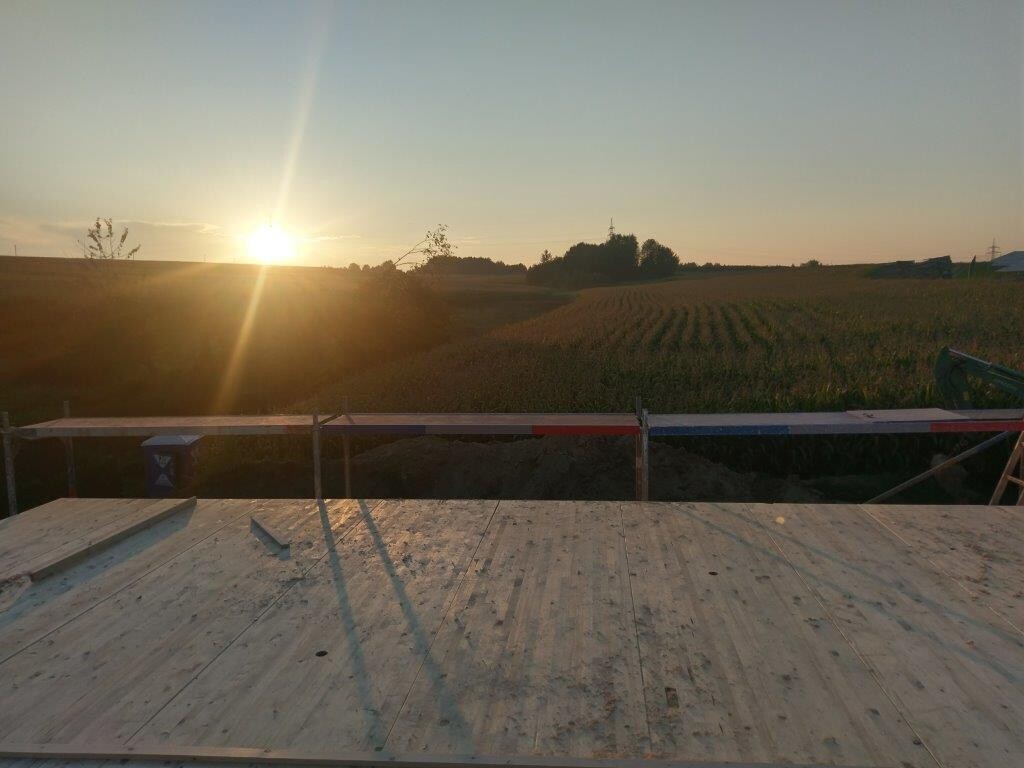 Sonnenuntergang über einer Holzplattform mit Bauzaun und Feldern im Vordergrund.