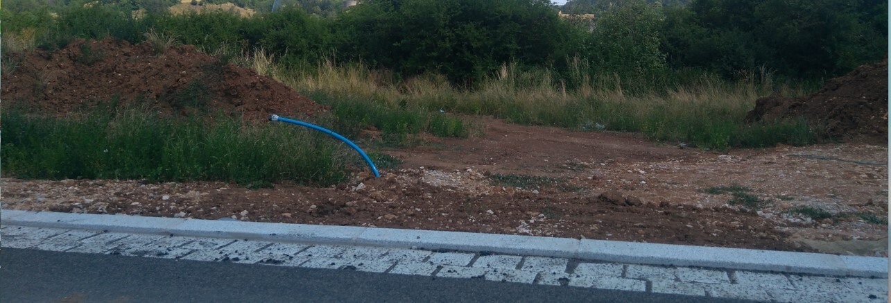 Straßenbaugebiet: blauer Schlauch ragt aus Erde; Kies, Randstein, Gras im Hintergrund.