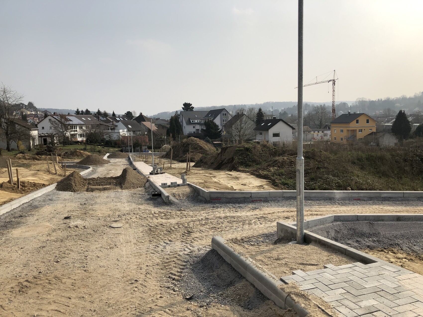 Baustelle in Wohngebiet: unbefestigte Wege, Erdhügel, Kran, Häuser im Hintergrund.