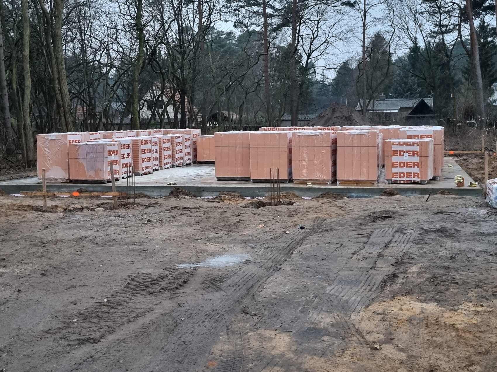 Baustelle mit pinkfarbenen Isolierplatten auf Fundamentplatte, Wald im Hintergrund.
