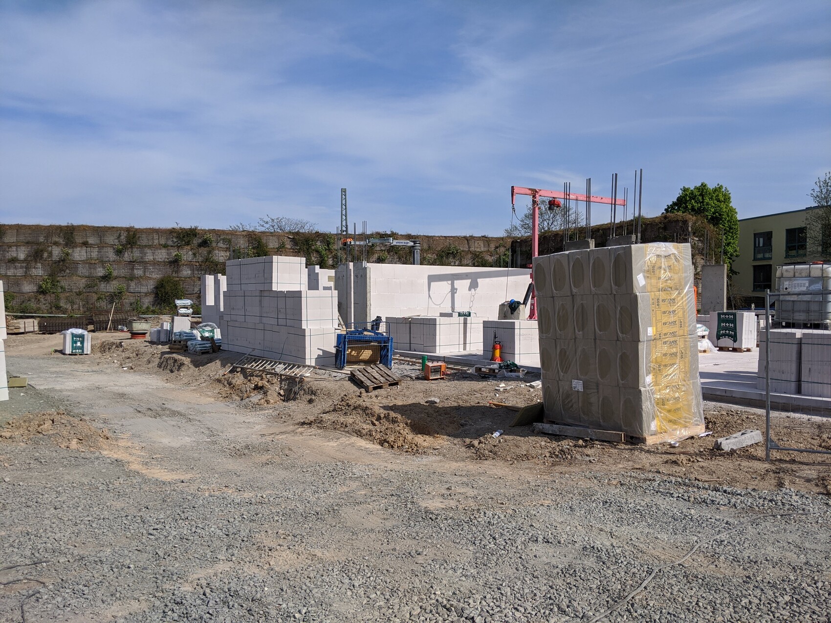 Bauplatz mit gestapelten weißen Betonblöcken, Kran, Paletten und Bauzubehör.