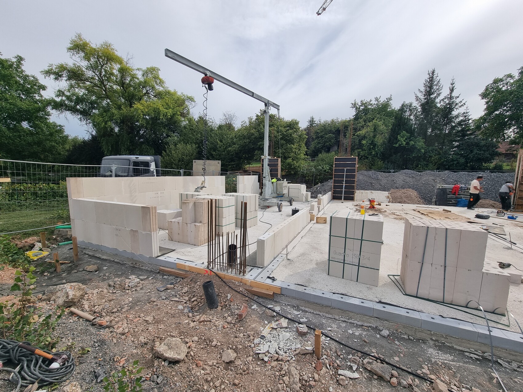 Baustelle mit Rohbaufundament, weiße Betonblöcke, Bewehrung und Kran