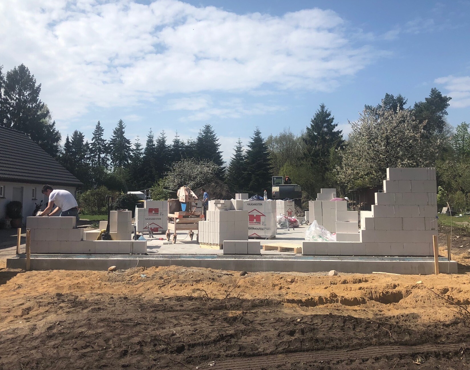 Baustelle mit gestapelten weißen Betonblöcken; Arbeiter errichten erste Wände eines Hauses.