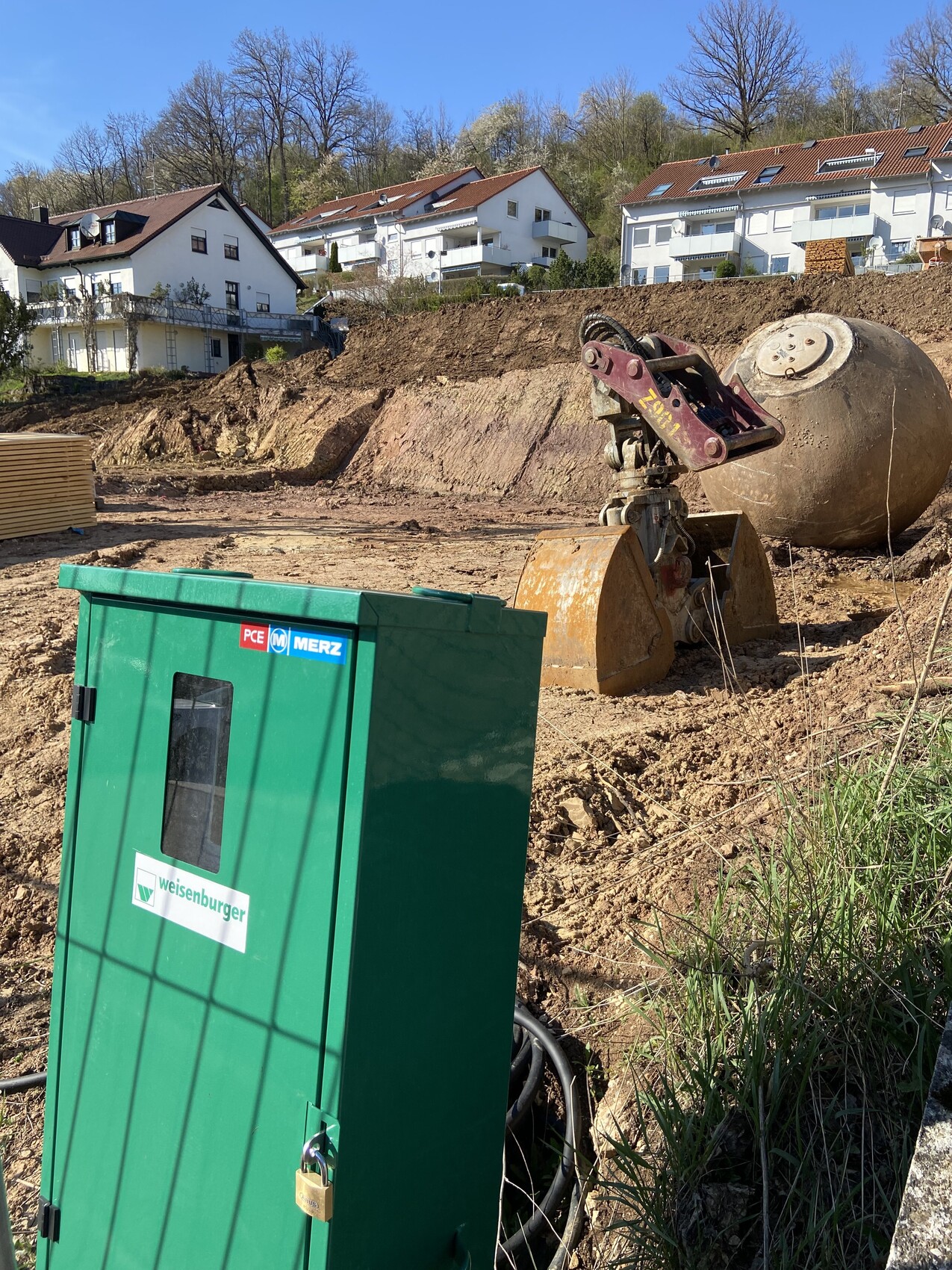 Baustelle mit Erdarbeiten, grüne Elektroverteilbox und Baugerät im Vordergrund