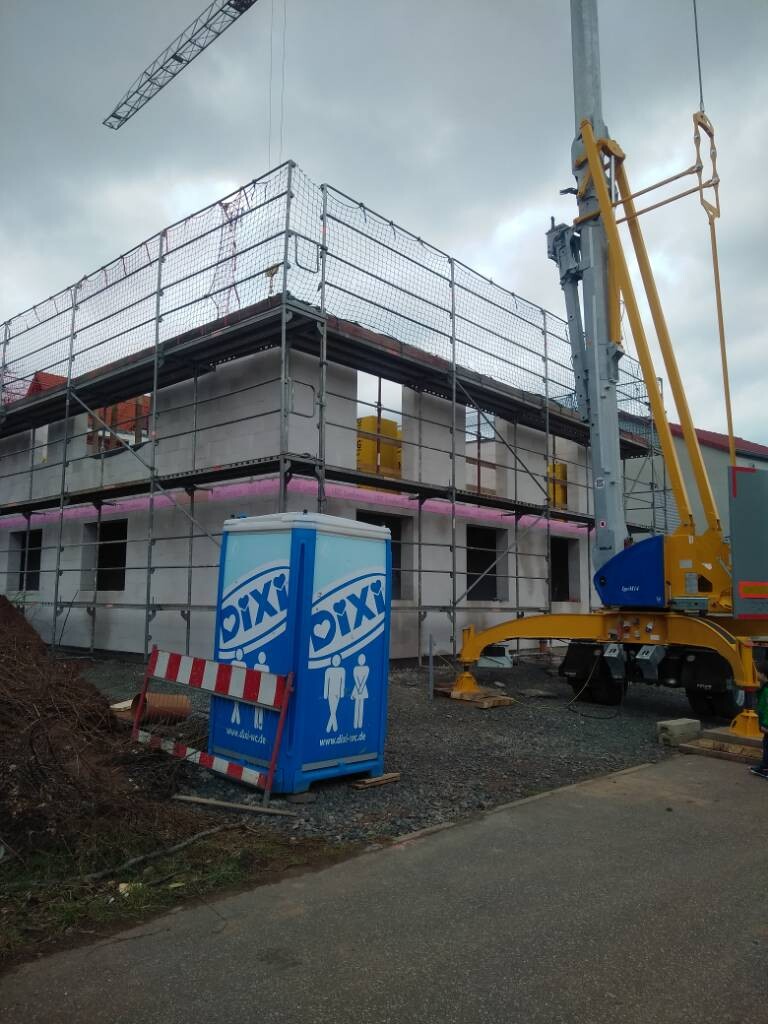 Baustelle mit Gerüst rund um ein Gebäude; blaue DIXI-Toilette im Vordergrund.