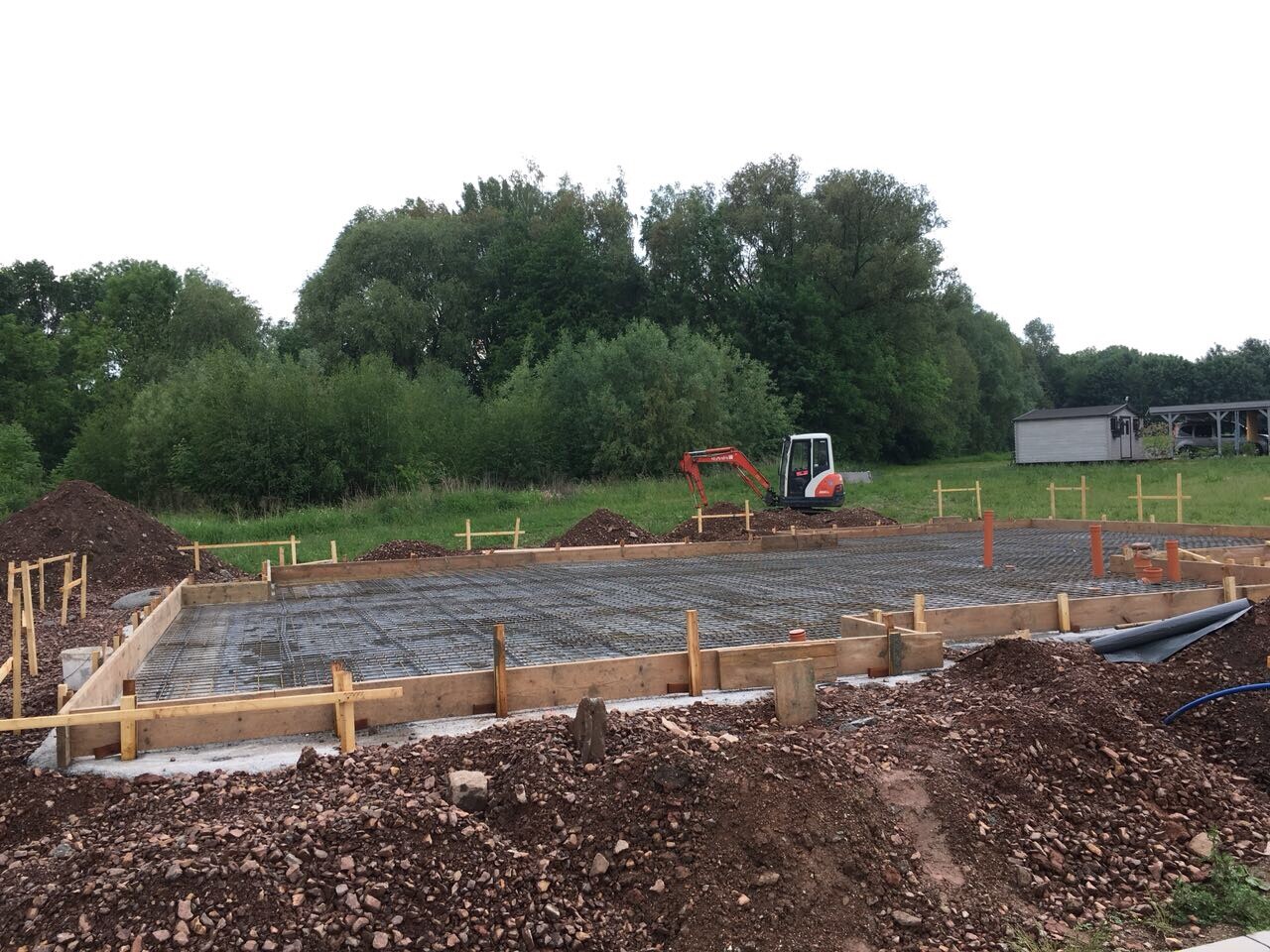 Baufundament mit Holzrahmen, Stahlbewehrung, Bagger im Hintergrund.