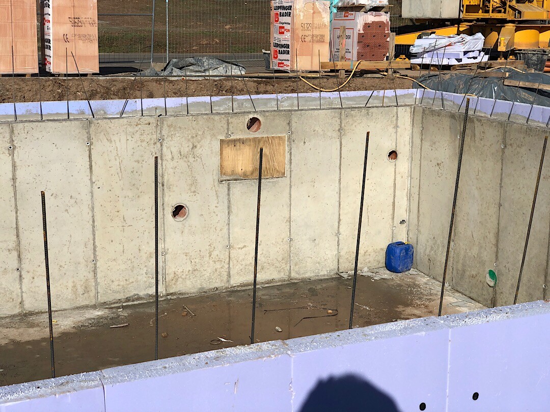 Baustelle mit Betonfundament, senkrechten Bewehrungsstangen und Baugeräten in einer Baugrube