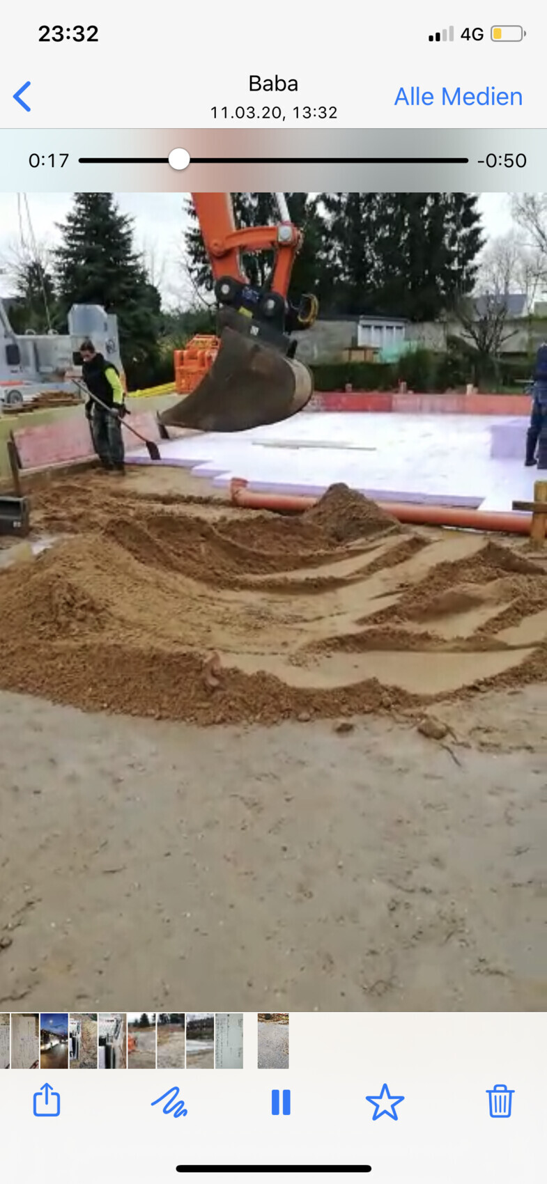 Baustelle: Bagger hebt Sandboden, Arbeiter mit Schutzweste daneben, Hintergrund Bäume.