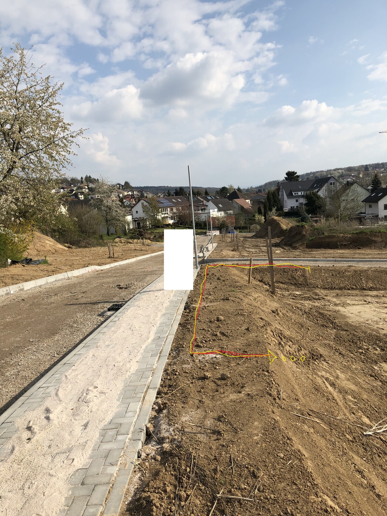 Neuer Gehweg aus Pflastersteinen links, Baufläche rechts, markiertes Baugebiet, Häuser im Umfeld