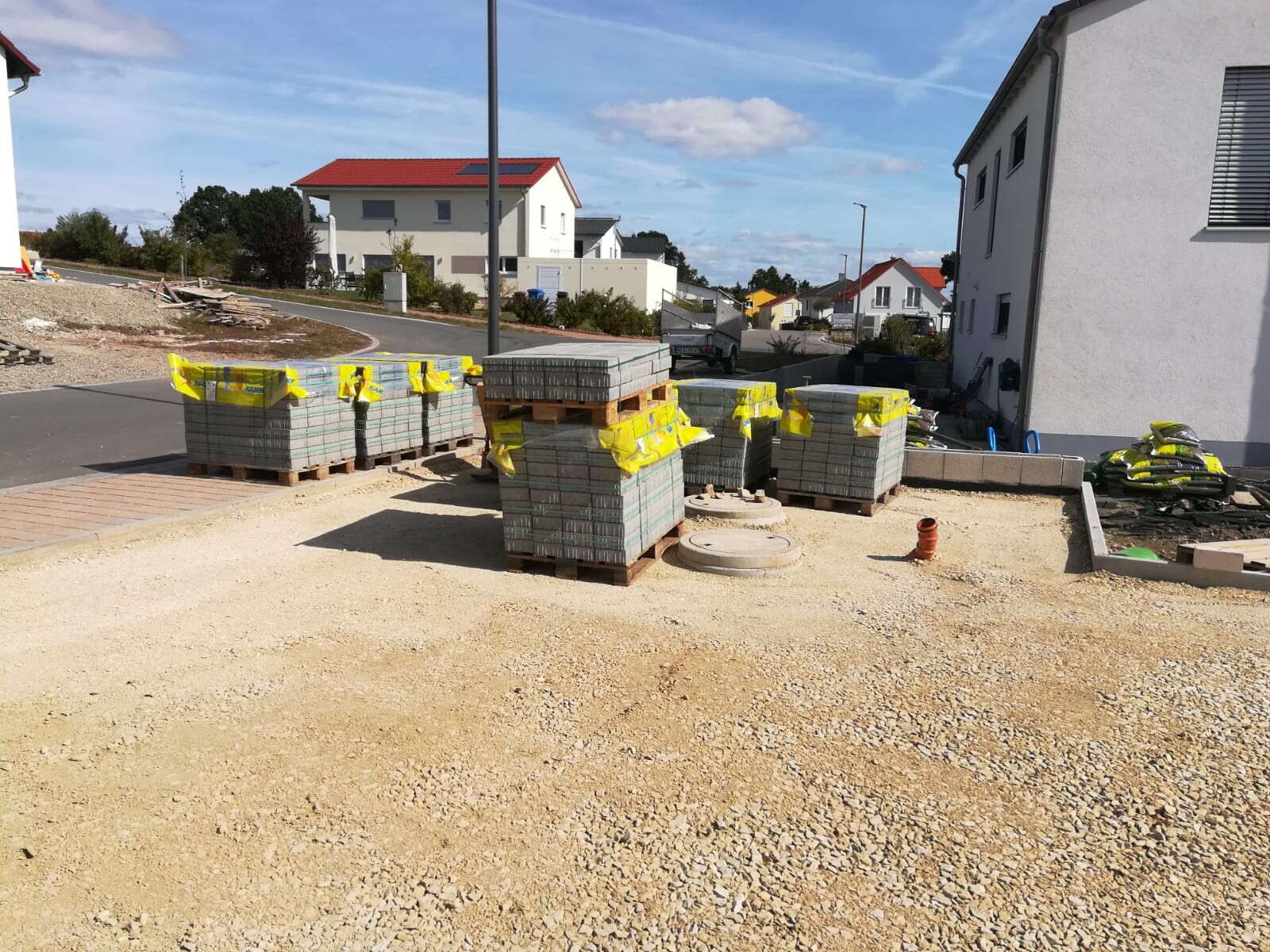 Baustelle in Wohngebiet: Paletten mit Pflastersteinen, gelbe Warnbänder, Kiesboden
