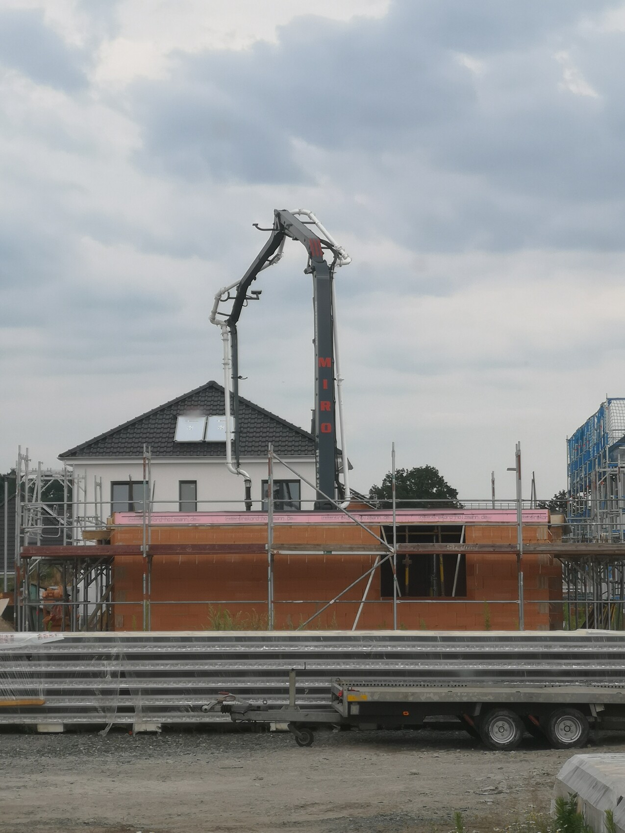Betonpumpenarm über Baugerüst vor orange Ziegelbau auf Baustelle, Haus im Hintergrund
