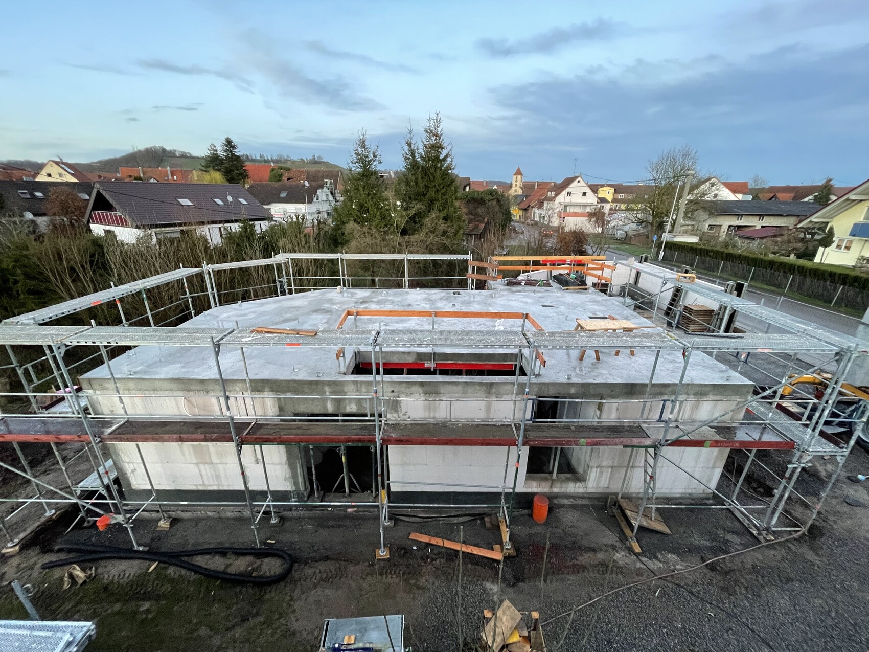 Blick von oben auf eine Baustelle: Gerüst um ein Neubau-Gebäude; Bauteile liegen auf dem Dach.