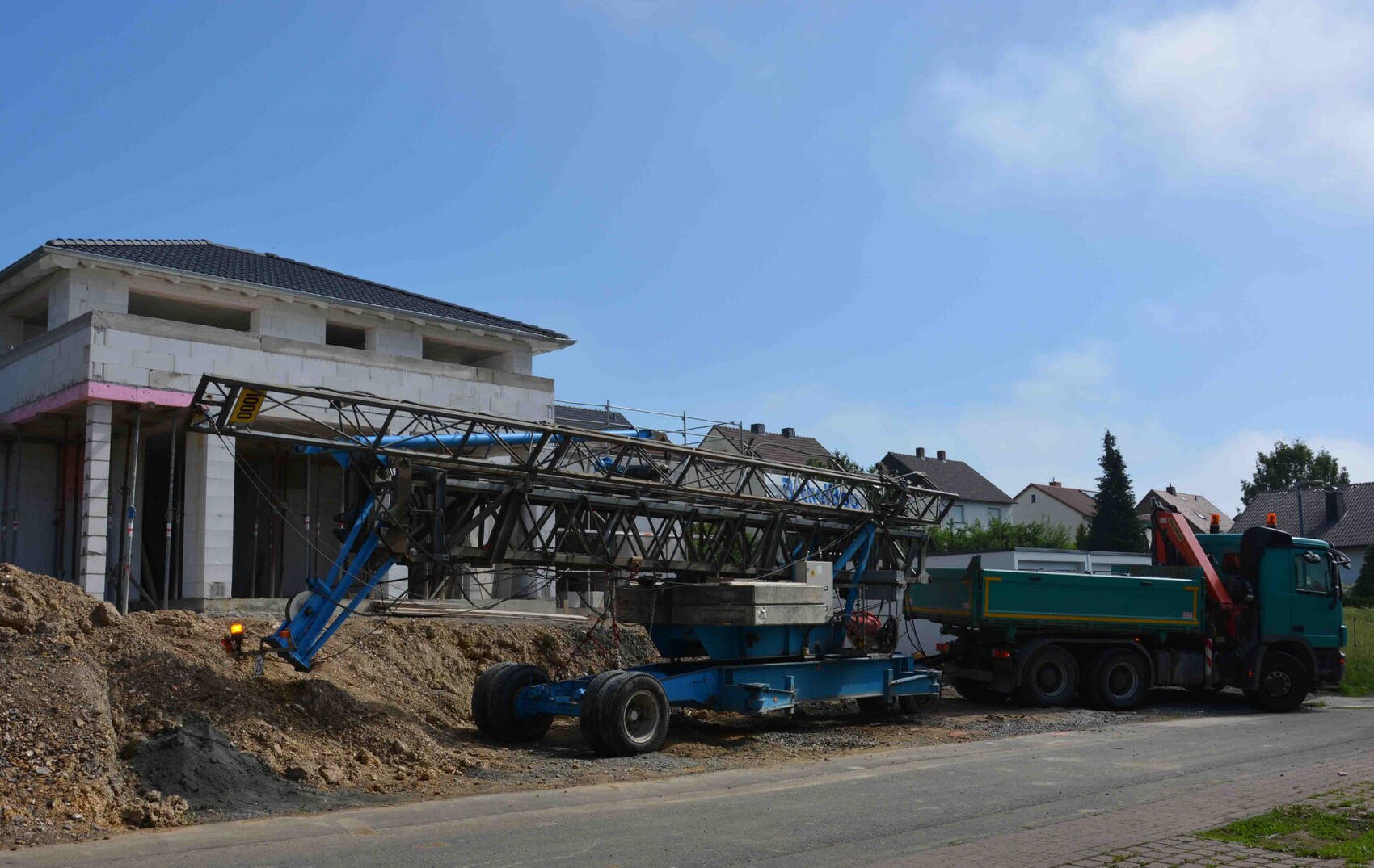 Große Baustelle: Baukran auf Trailer vor einem unfertigen zweistöckigen Haus, Erdarbeiten am Boden.
