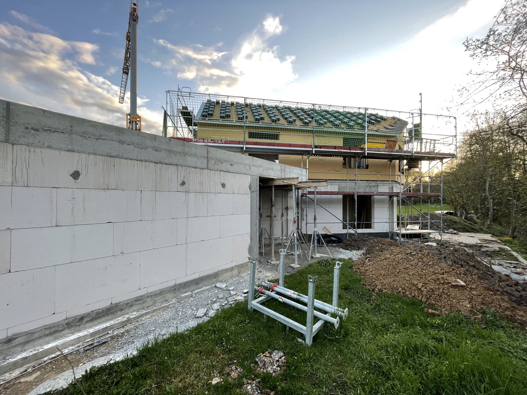 Baustelle mit Rohbau, Gerüst, Kran links, Betonwand im Vordergrund, Erdaushub