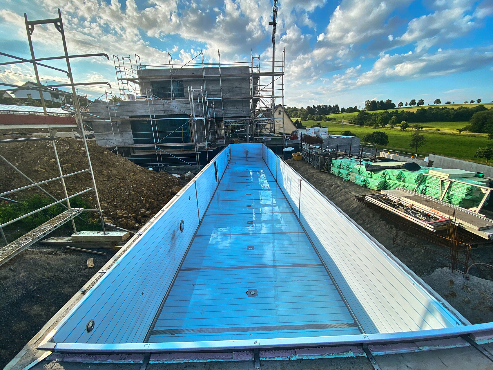 Rohbau-Baustelle mit Gerüsten, blauem Becken und grüner Landschaft im Hintergrund