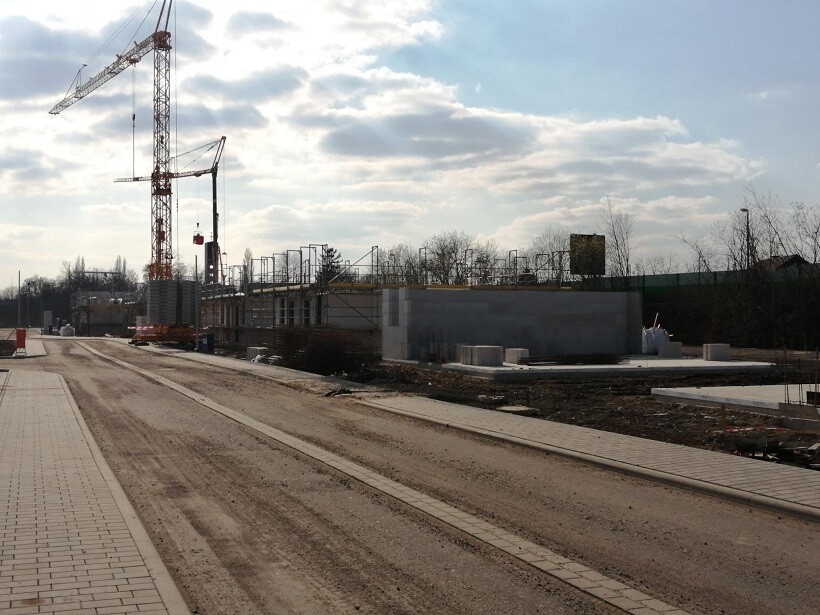 Baustelle mit Kran links, Gebäudebau im Gange, Straße und Gehweg im Vordergrund