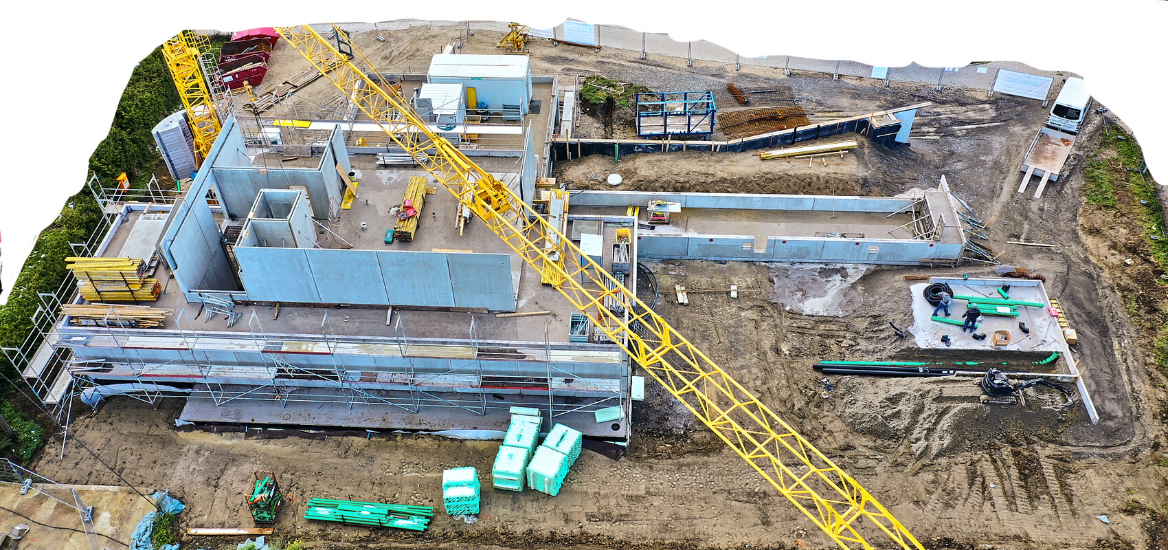 Große Baustelle mit gelbem Kran, blauen Betonwänden, Gerüst, Bauarbeitern und Materialien.