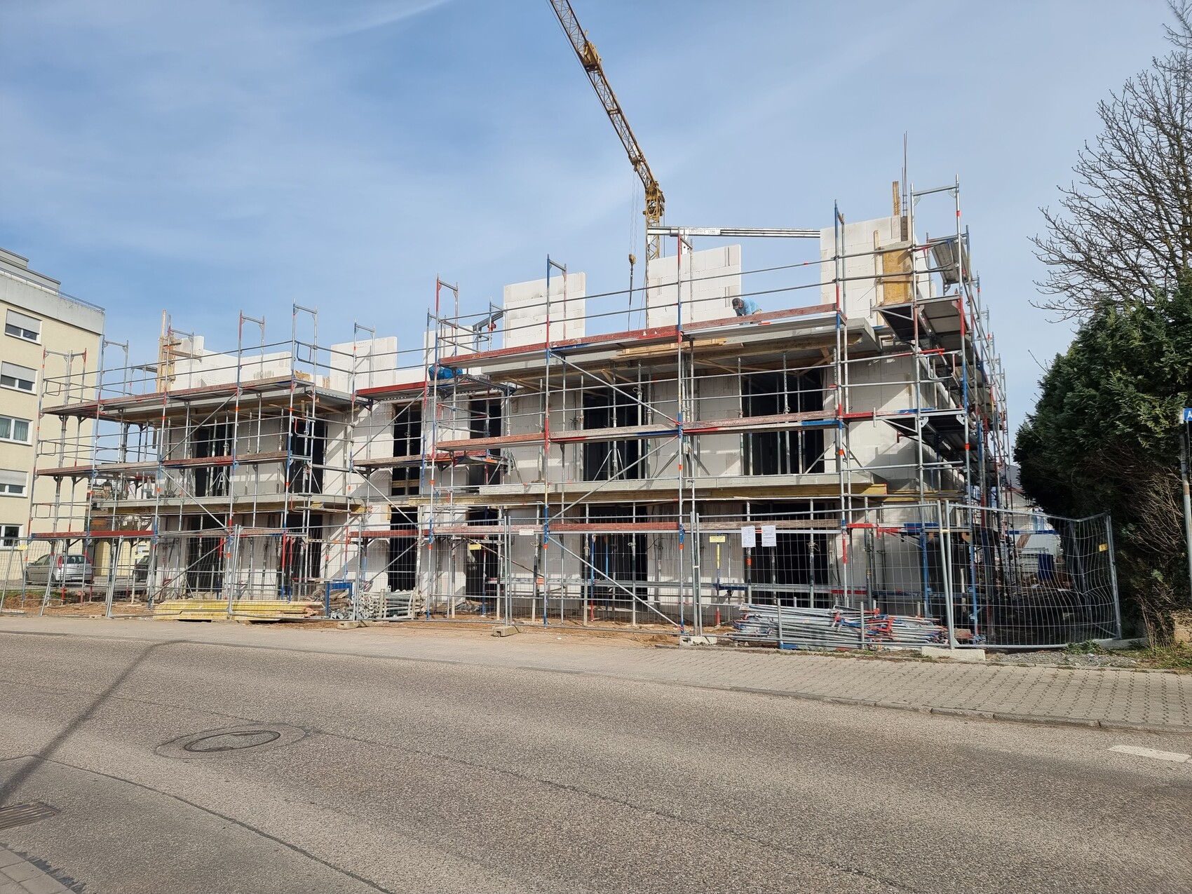 Mehrstöckiges Bauvorhaben: Rohbau mit Gerüst, Kran über der Baustelle und Straße davor.