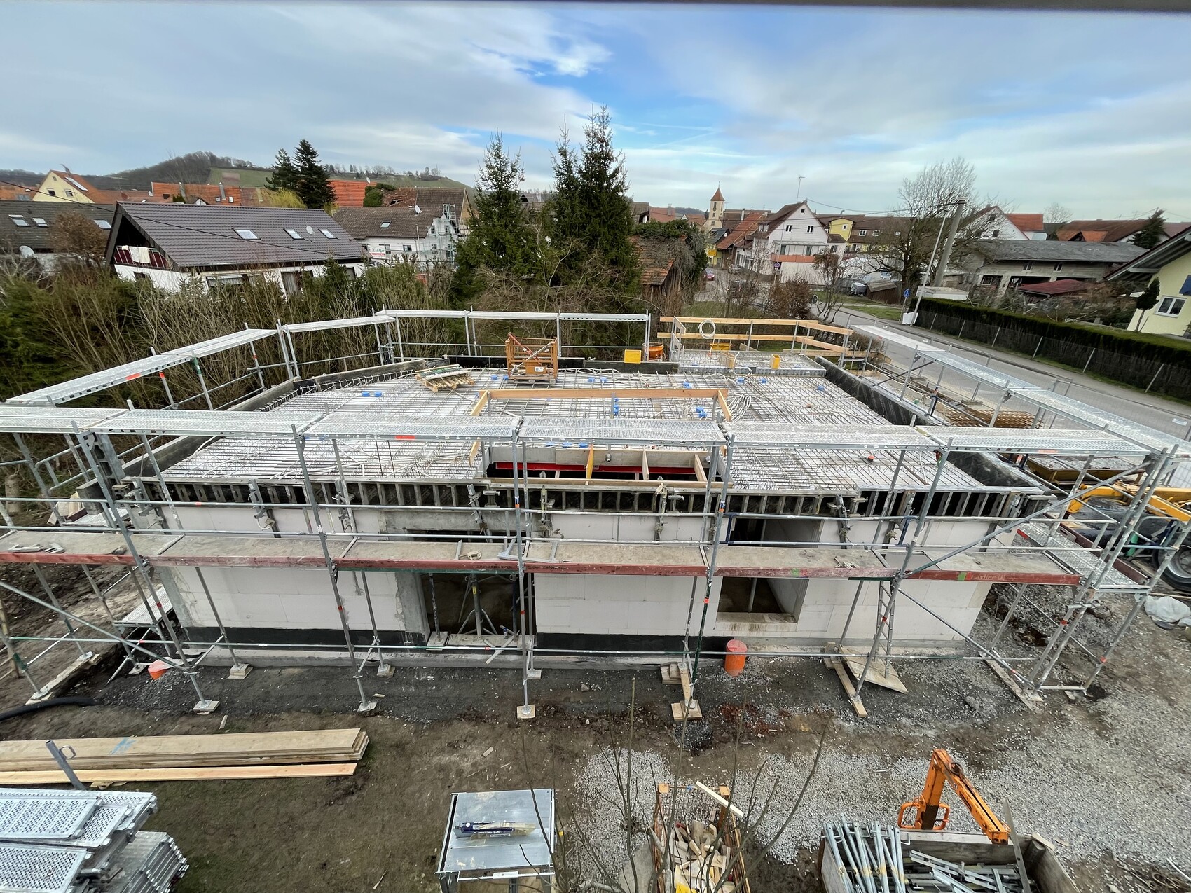 Baustelle eines Wohnhauses mit Gerüst, Stahlbewehrung auf dem Dach und Baumaterialien.