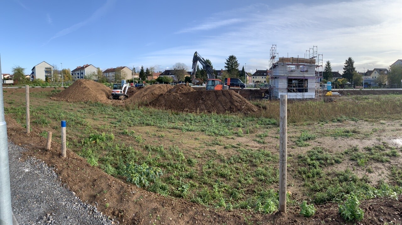 Baufeld mit Erdhaufen, Bagger, Gerüstbau an einem Neubau in einer Wohngegend.
