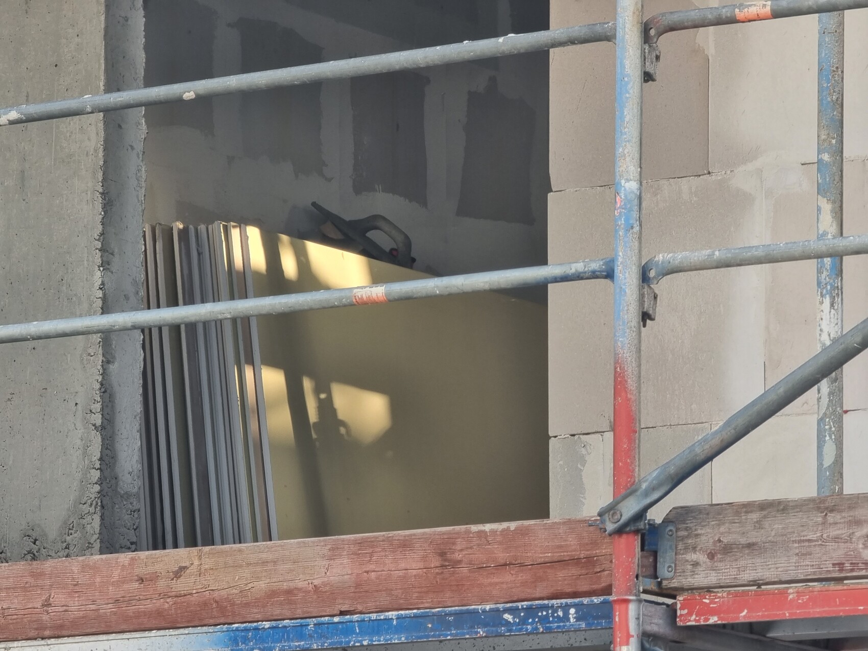 Baustelle mit Gerüst, Holzplanken am Boden und stapelbaren Metallplatten neben einer Wand.