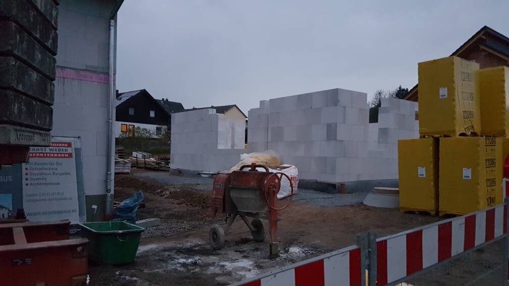 Baustelle mit weißen Betonblöcken, rotem Betonmischer, gelben Kartons und Absperrband.