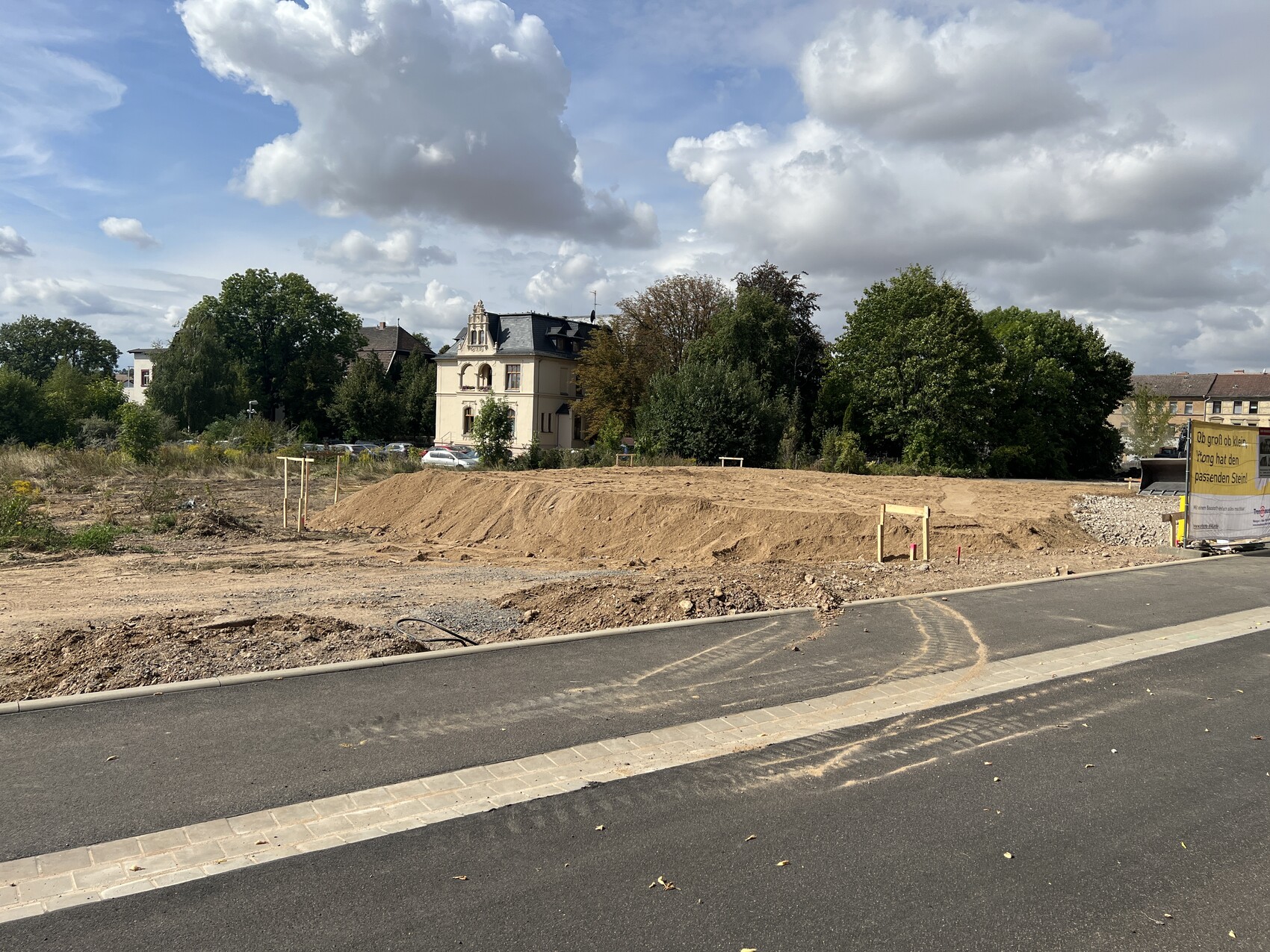 Baustelle mit Erdarbeiten, Sandhügeln, Baugrube und Gebäude im Hintergrund