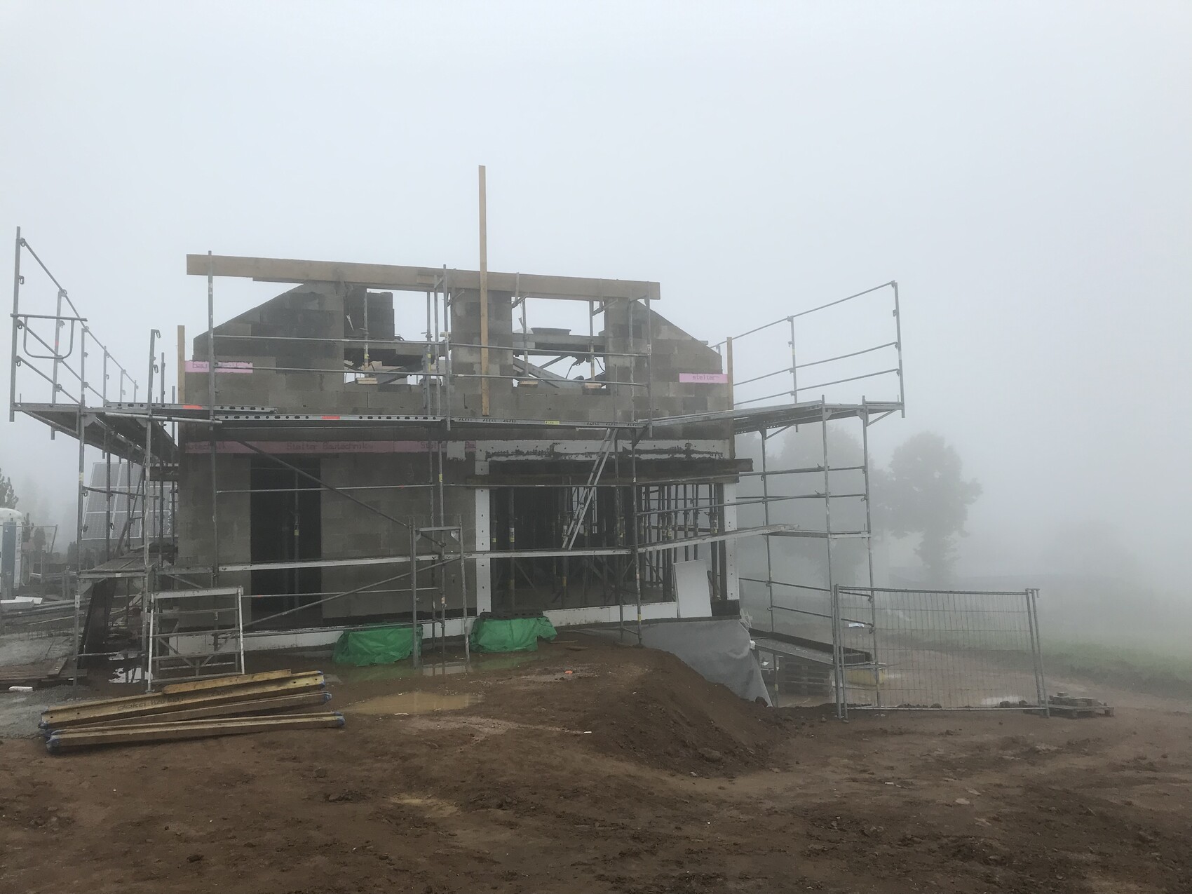 Baufeld mit Gerüst um ein unfertiges Haus, Nebel, Bauholz, Schlamm und Baumaterialien.