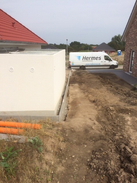 Baustelle mit weißer Rohbauwand, Erdarbeiten und Hermes-Lieferwagen am Haus