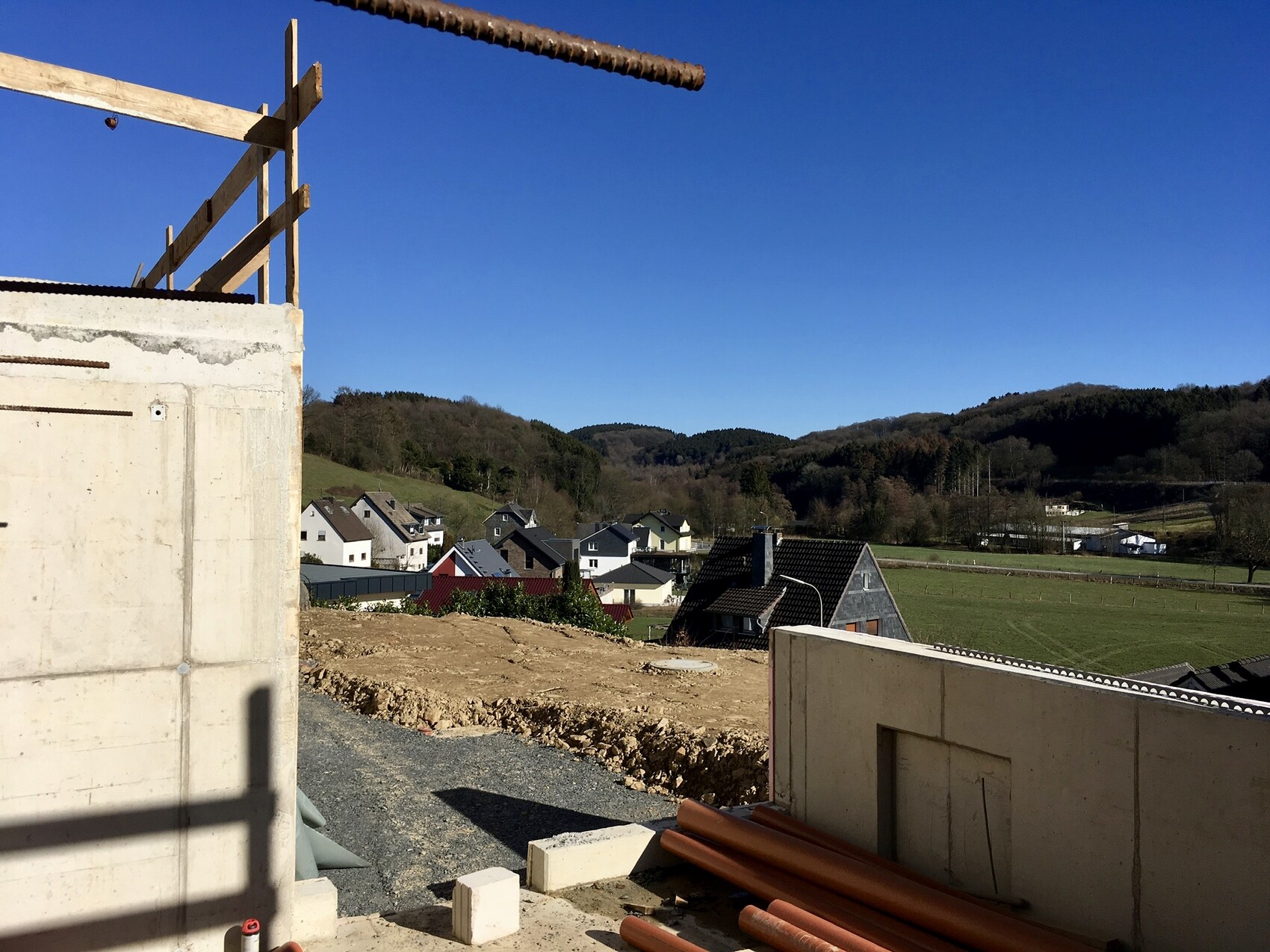 Baustelle mit Betonwand und Holzrahmen im Vordergrund; Dorflandschaft mit Hügeln im Hintergrund