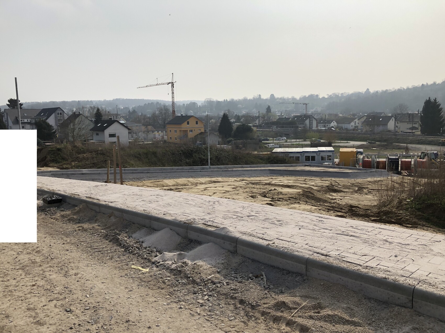 Bauplatz mit Pflasterweg, Erdarbeiten, Kran im Hintergrund und Vorstadthäusern.
