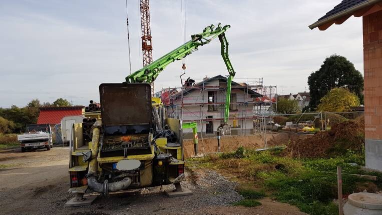 Baustelle mit grünem Betonpumpenarm, Baugerüst und Baufortschritt am Haus.