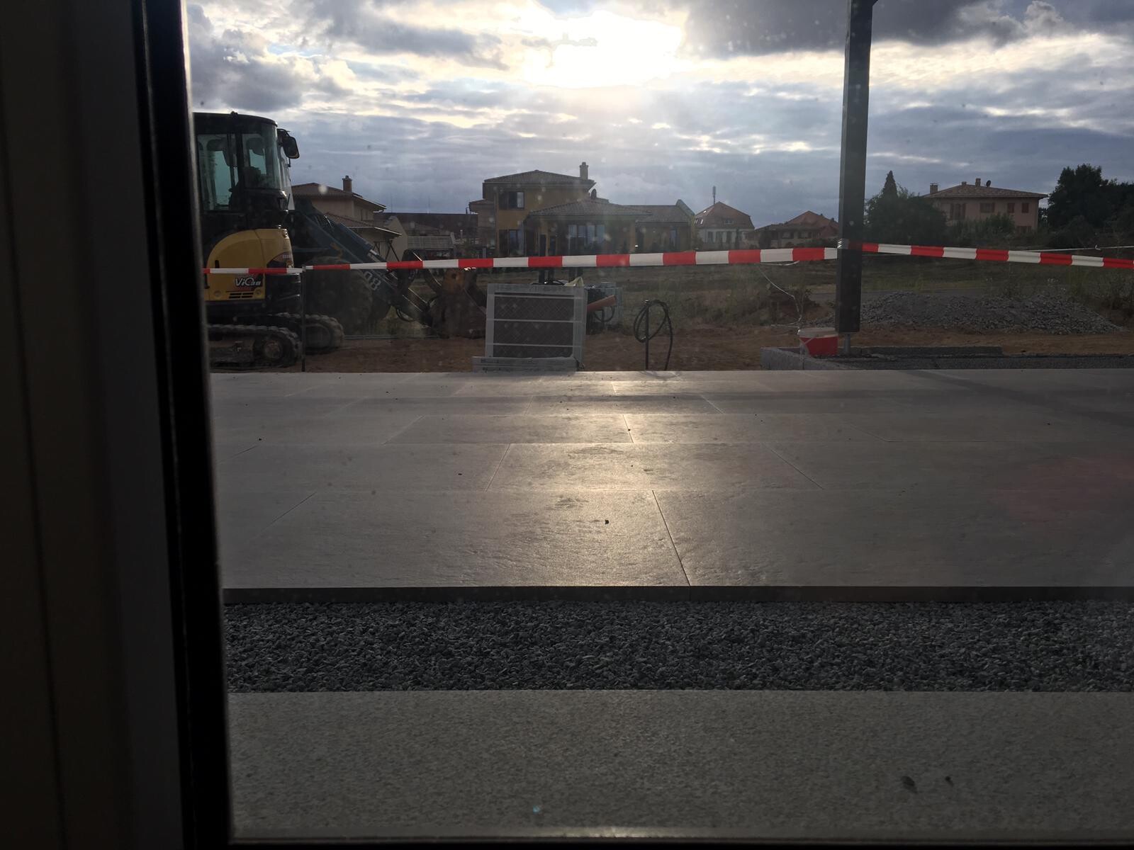 Blick auf eine Baustelle mit Bagger hinter Absperrband und Häusern im Hintergrund.