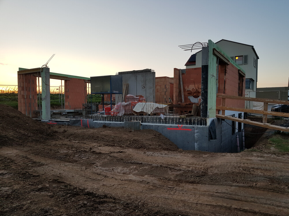 Unfertiges Haus auf Baustelle mit Ziegelwänden, Betonfundament und Baumaterialien.