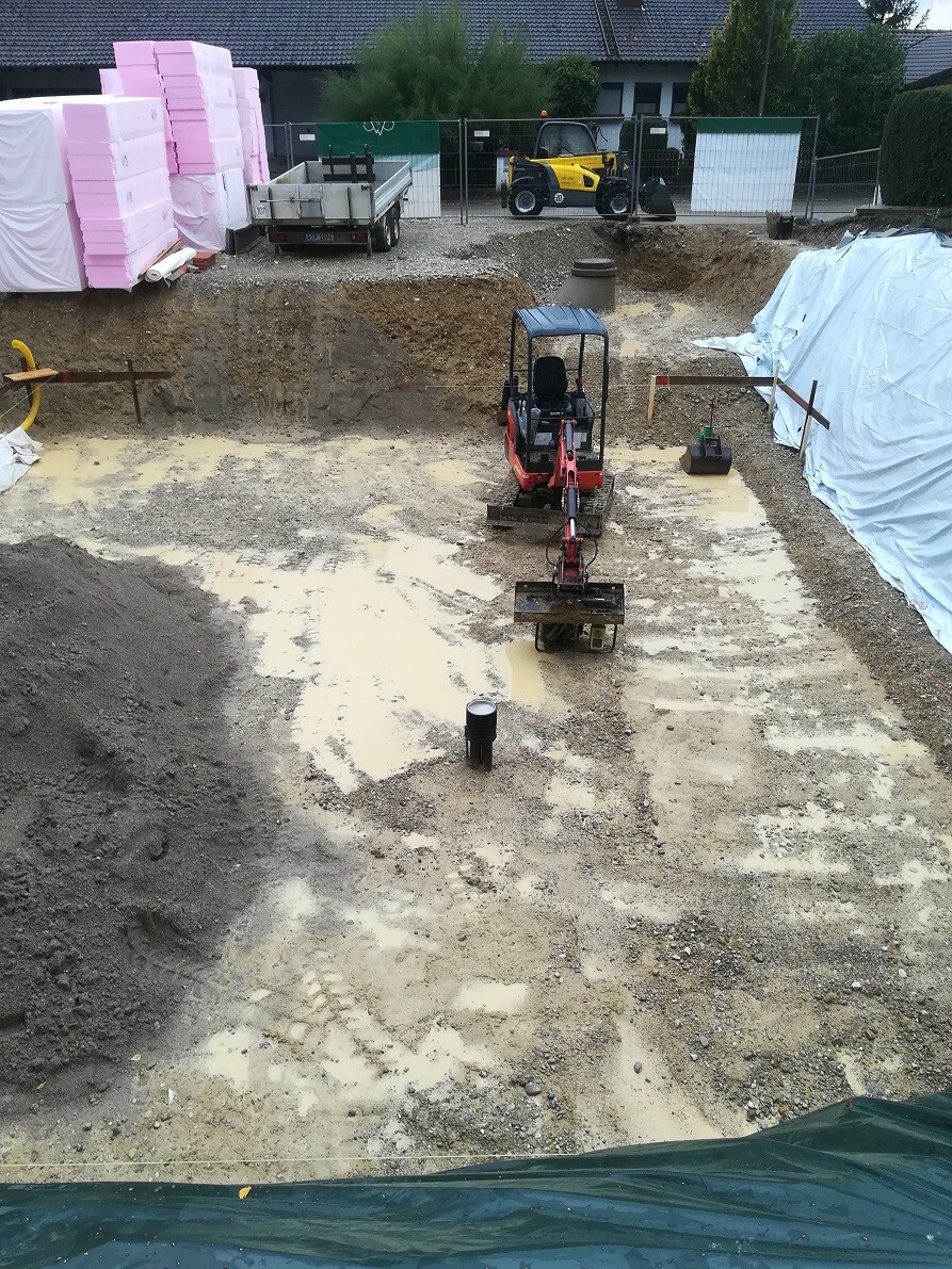 Kleine Baustelle mit Mini-Bagger in Grube, Erde, Planen und Bauutensilien sichtbar.